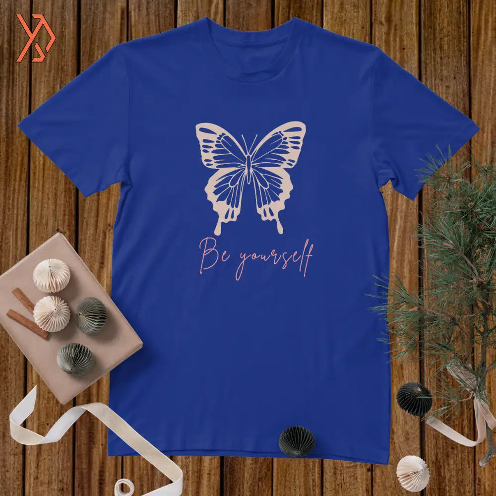 Blue t-shirt with a butterfly and 'Be yourself' text on a wooden surface.
