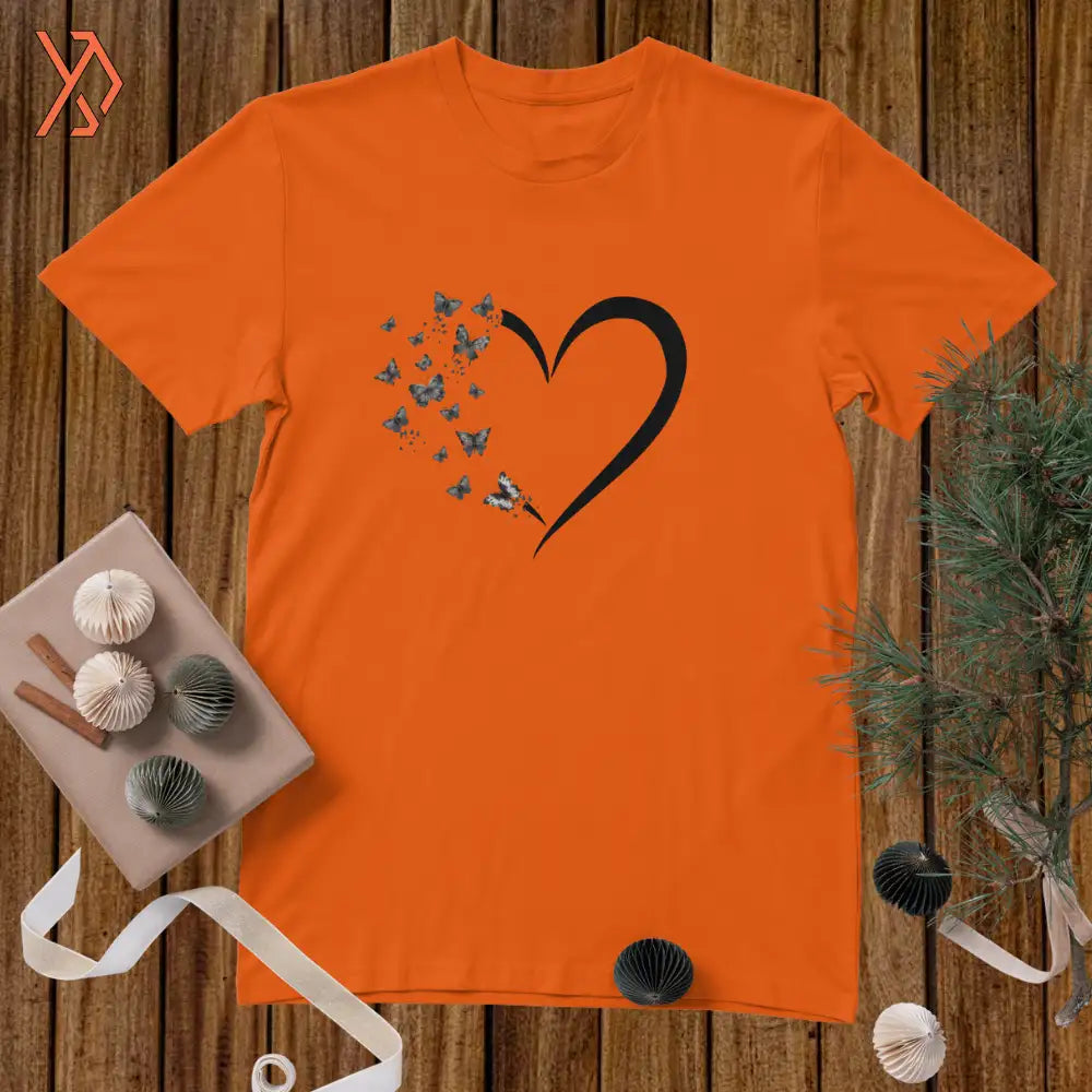 Orange t-shirt with a black heart and butterfly design on a wooden surface.